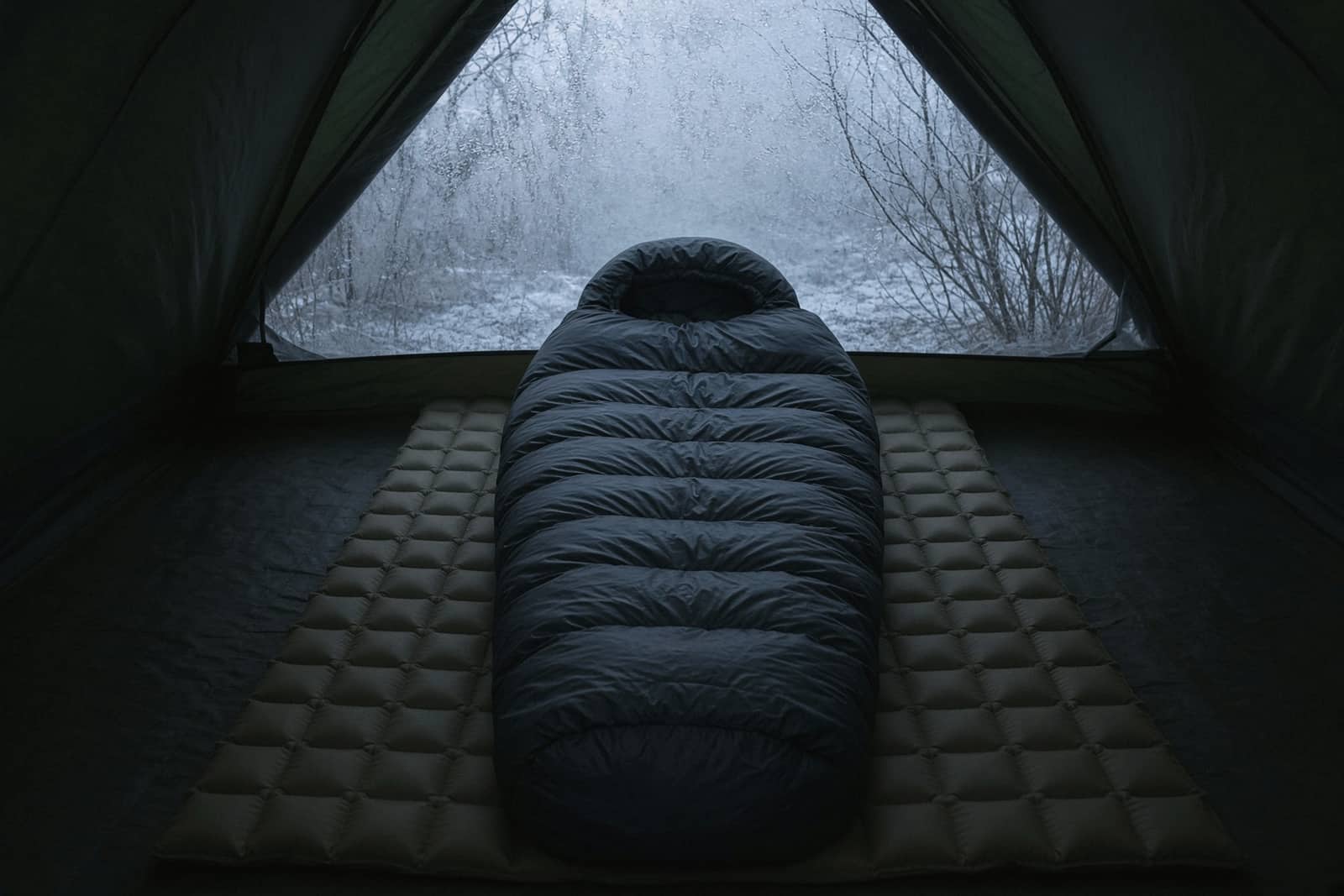 A thick hooded down bag on a high-insulation pad inside a tent with a frost-rimed fly, dawn