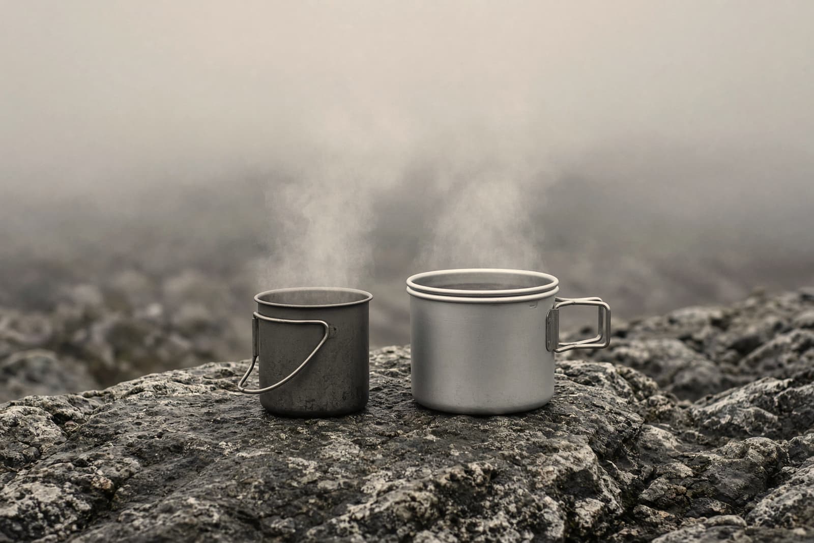 A titanium solo pot and a larger aluminum pot side by side on a stone, light steam