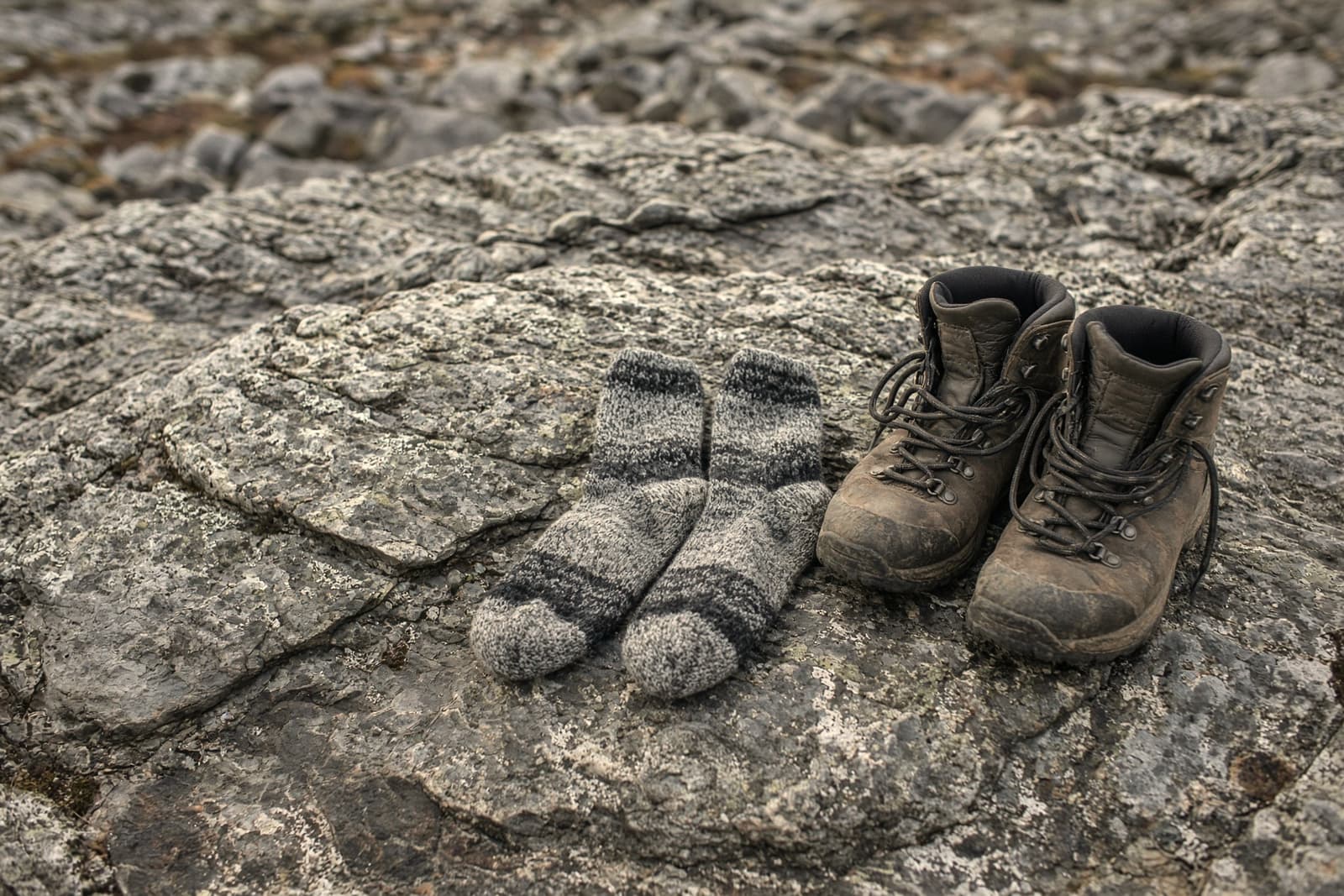 Wool hiking socks drying on a sun-warmed rock beside a pair of unlaced boots