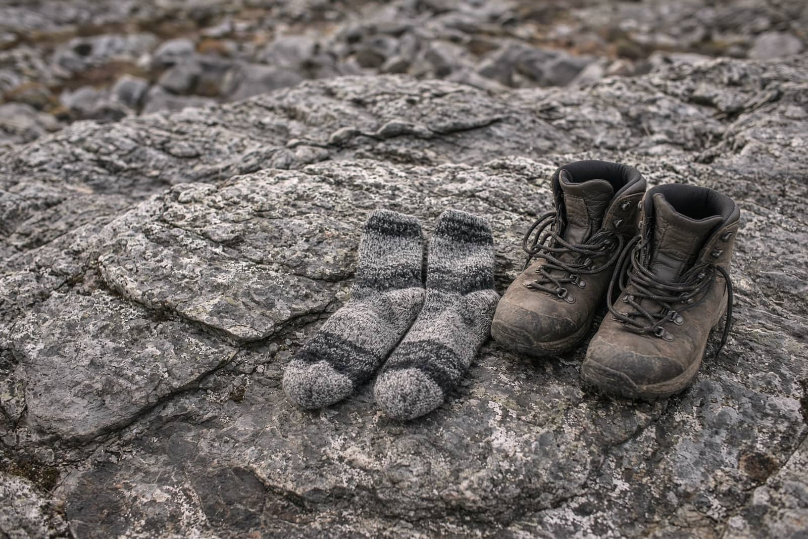 Wool hiking socks drying on a sun-warmed rock beside a pair of unlaced boots