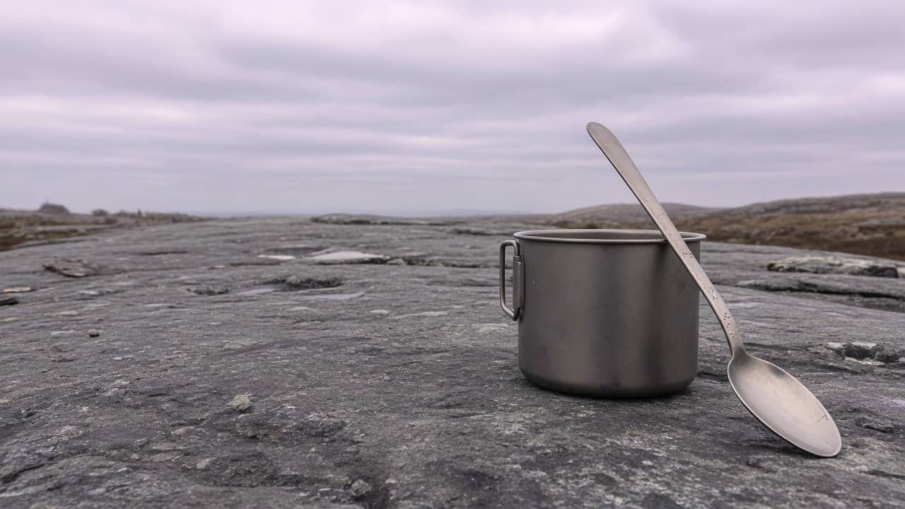 A titanium pot and a long spoon on a stone in the right half, darker rock on the left