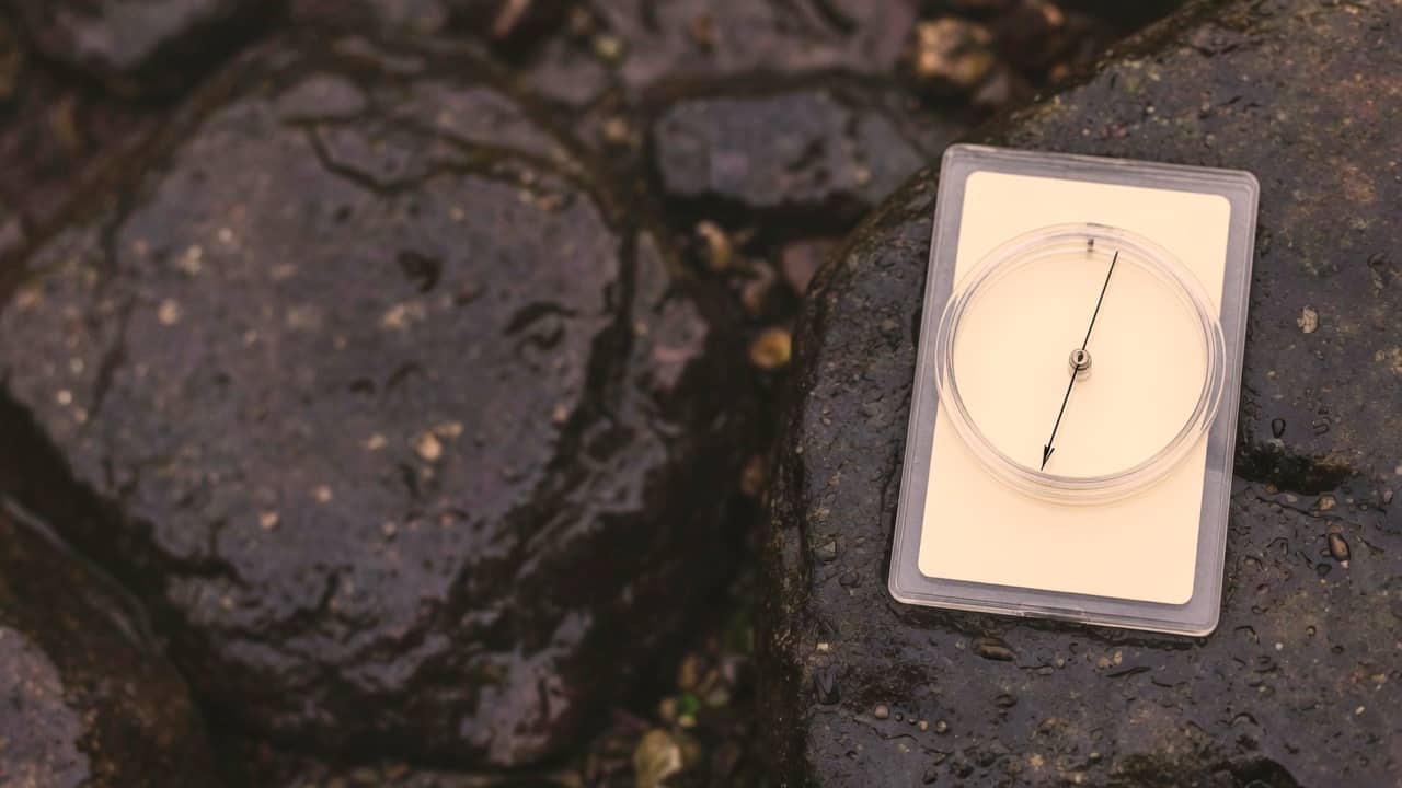 A blank baseplate compass on dark wet rock, sitting in the right quarter of the frame