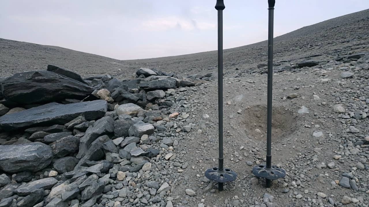 Two trekking poles with baskets planted in scree on the right, quieter talus on the left