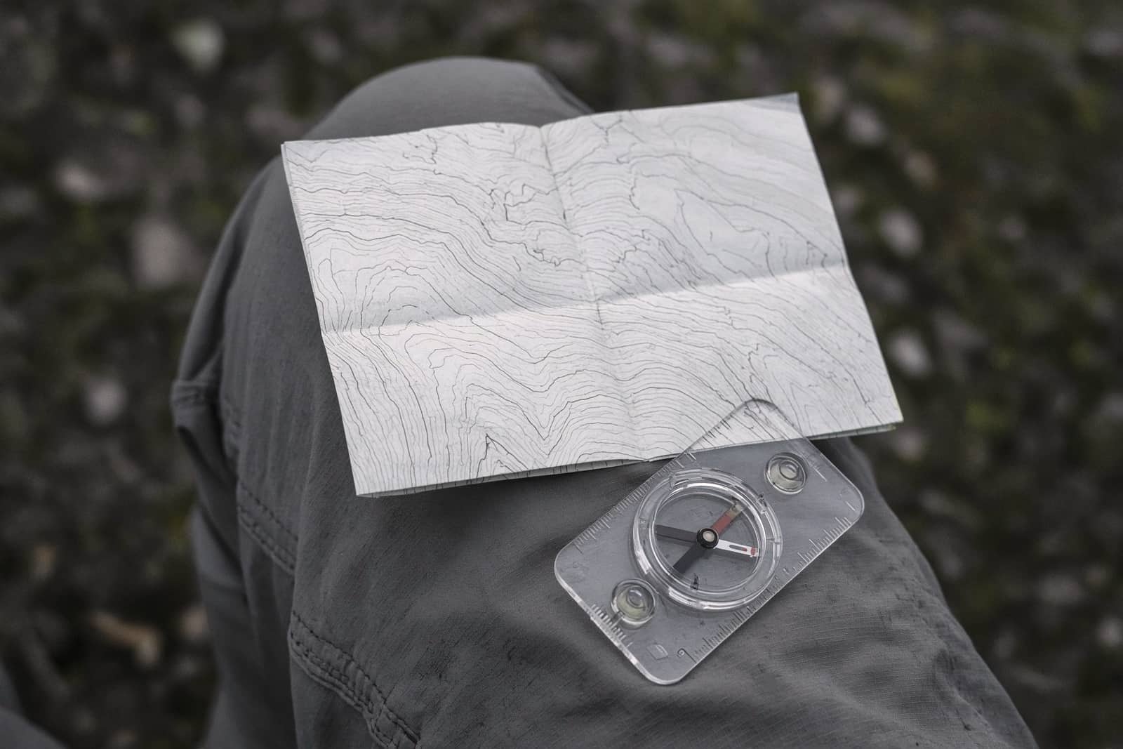A topo map and baseplate compass on a hiker's knee, contour lines soft and unreadable