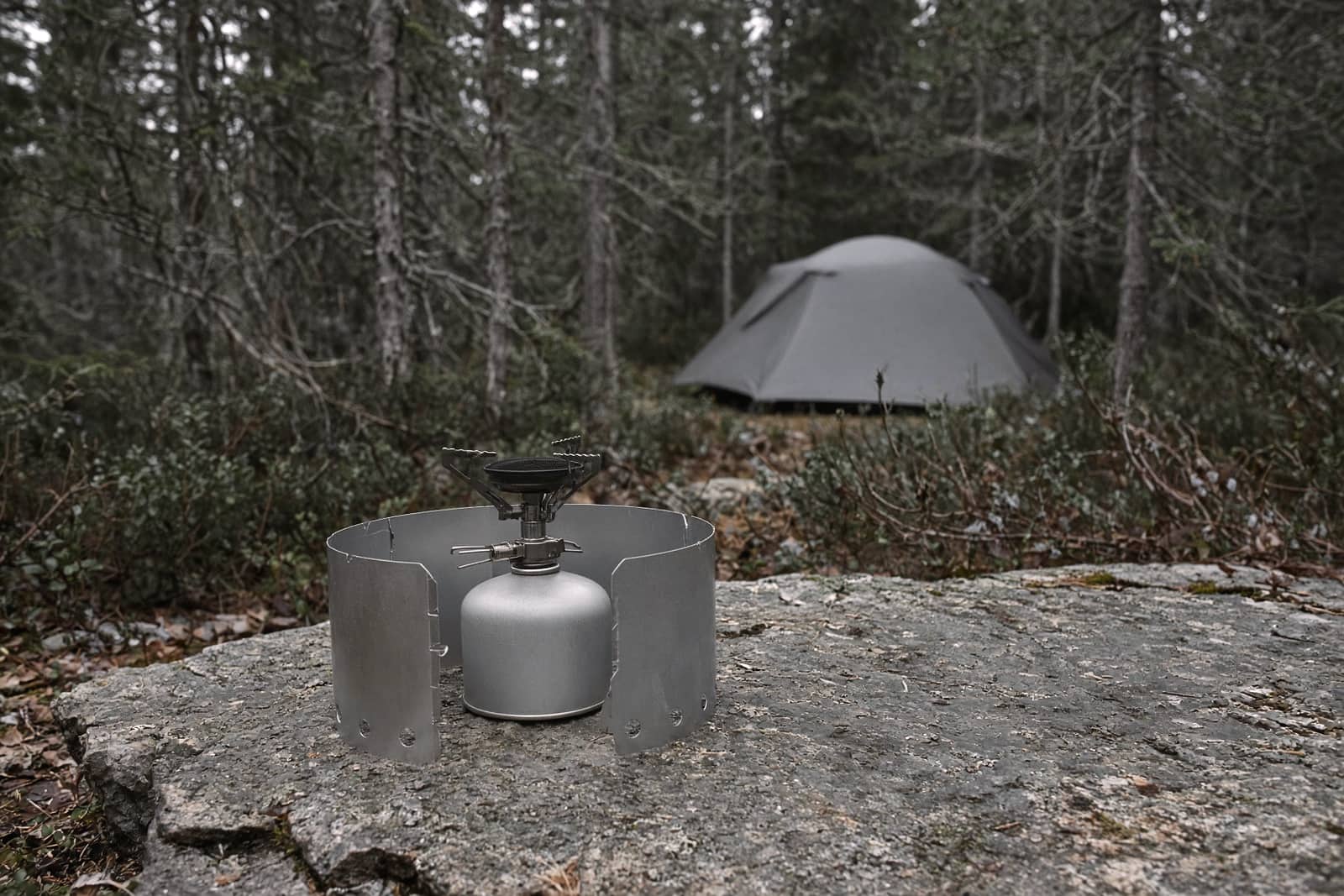 A canister stove with a windscreen on a stable flat rock, well away from the tent vestibule