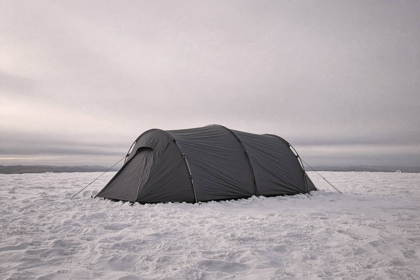 A low four-season dome tent on wind-scoured snow under a grey sky