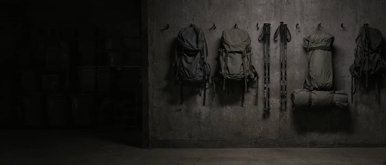 A gear wall in a dim garage: packs, poles and tents on hooks