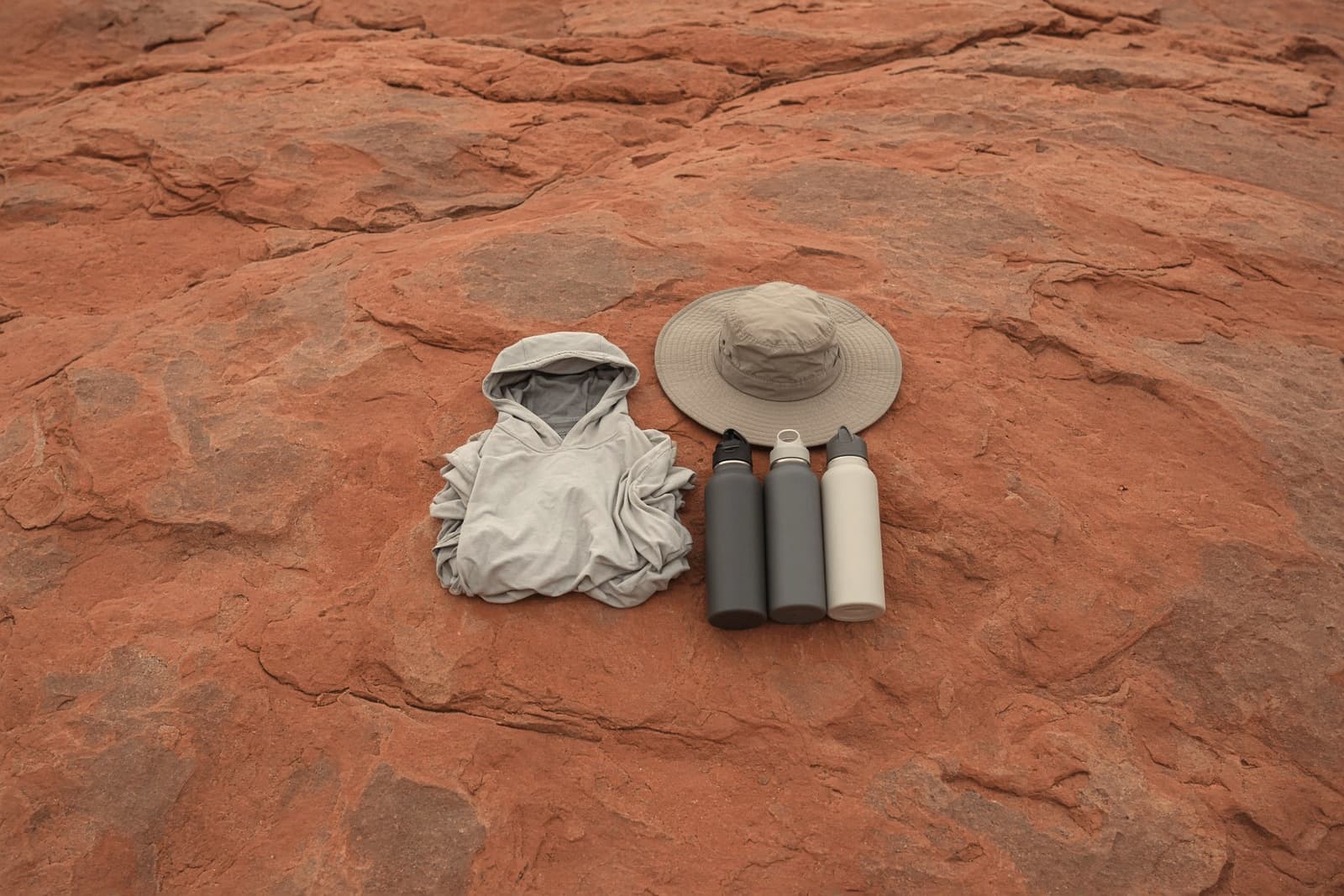 A sun hoodie, a wide-brim hat and three water bottles on slickrock