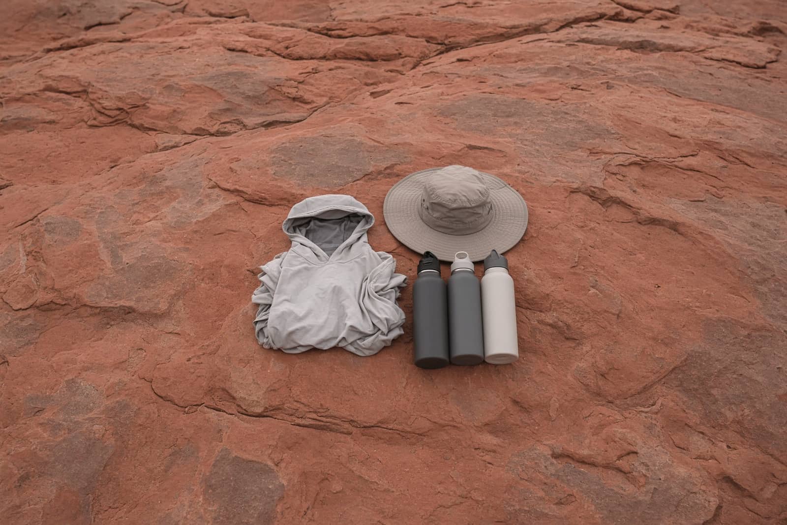 A sun hoodie, a wide-brim hat and three water bottles on slickrock