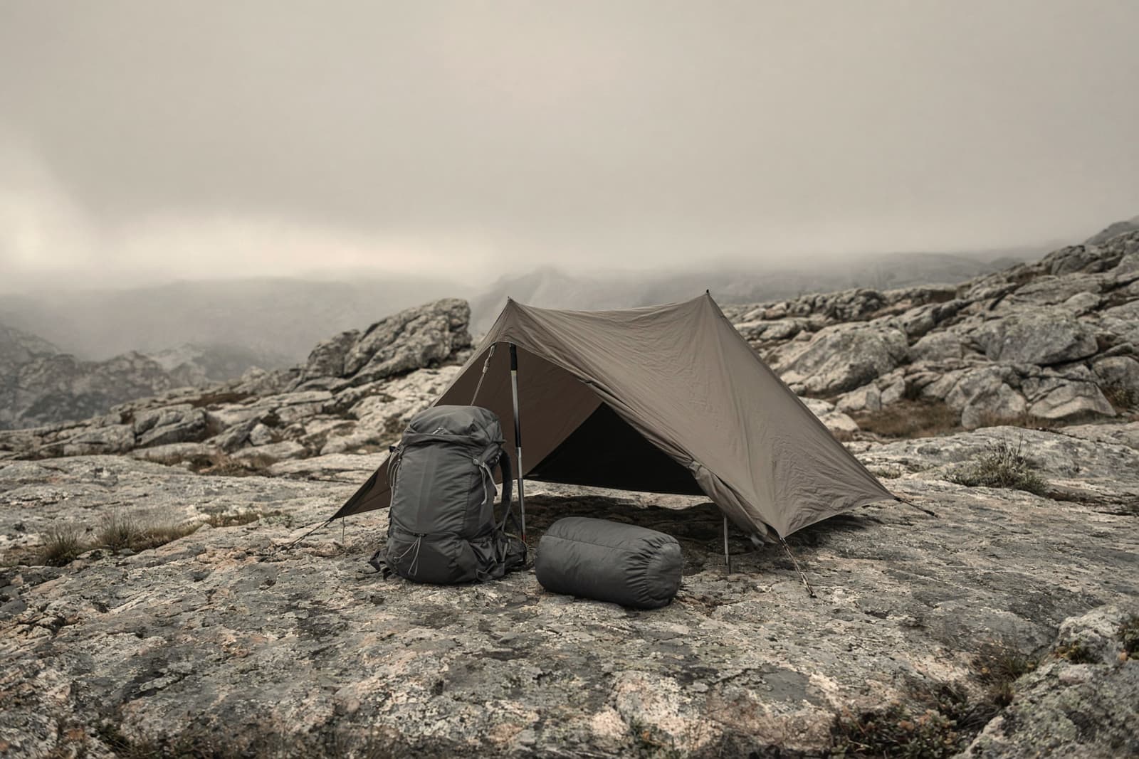 A trimmed ultralight kit on a granite slab: small pack, pole shelter, quilt