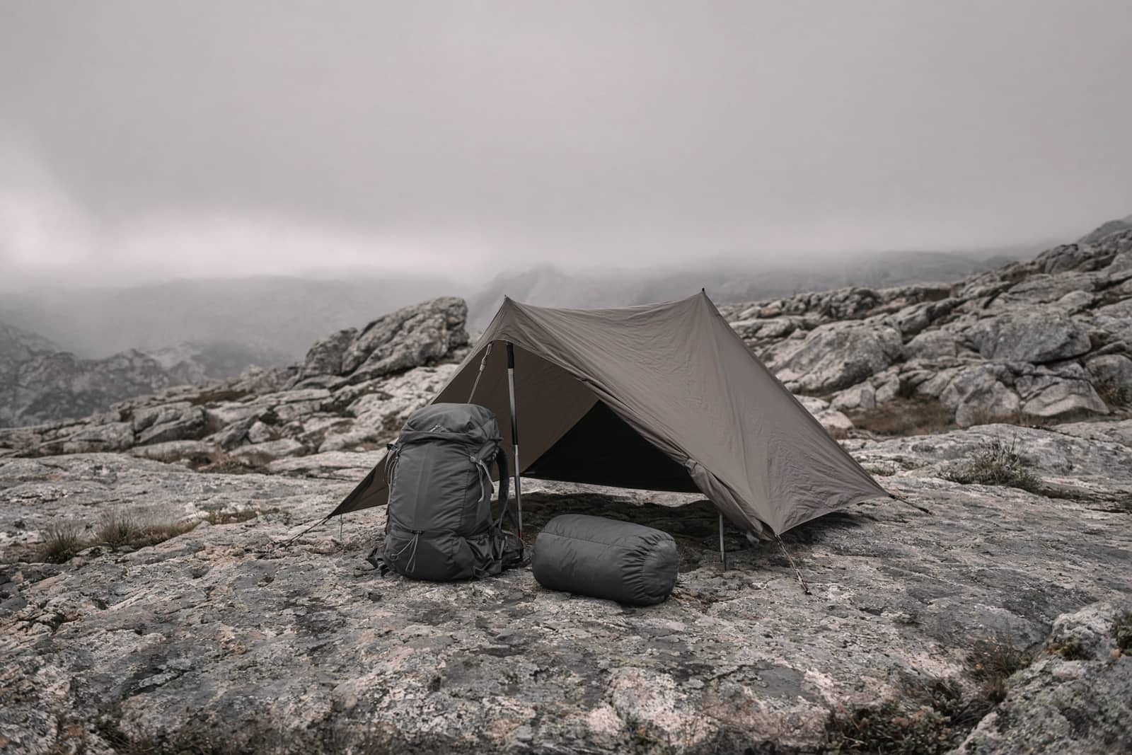 A trimmed ultralight kit on a granite slab: small pack, pole shelter, quilt