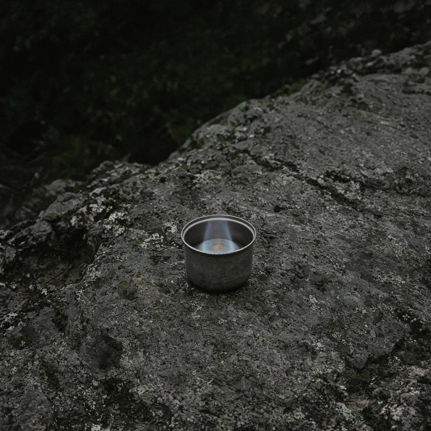 A tiny alcohol stove with a faint flame on bare rock