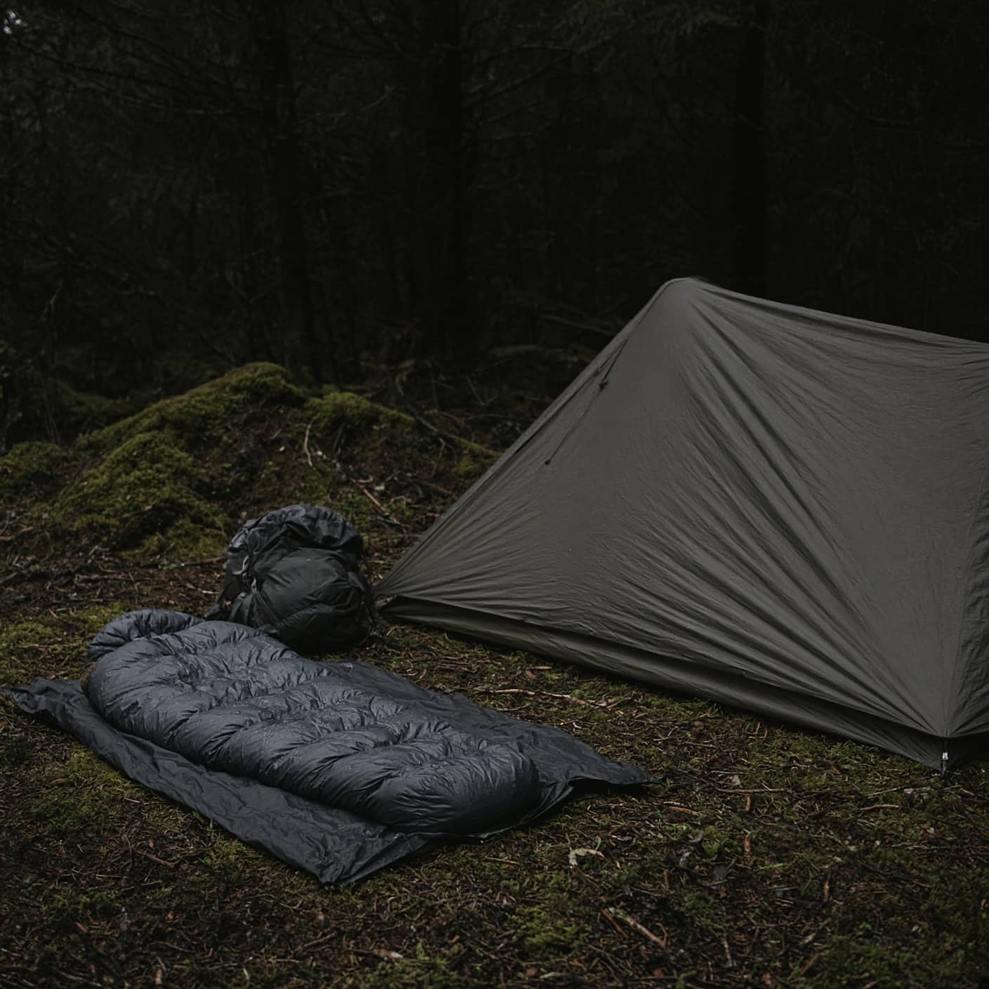 A tent, a sleeping bag and a pack together on a groundsheet