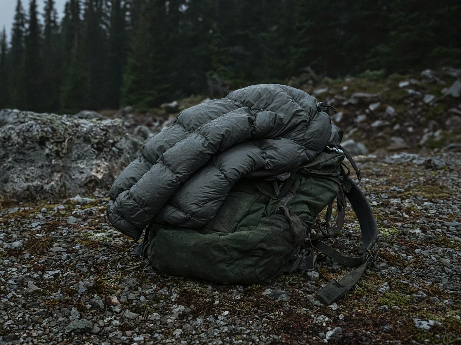 An ultralight down jacket stuffed in its pocket draped over a pack at a cold camp
