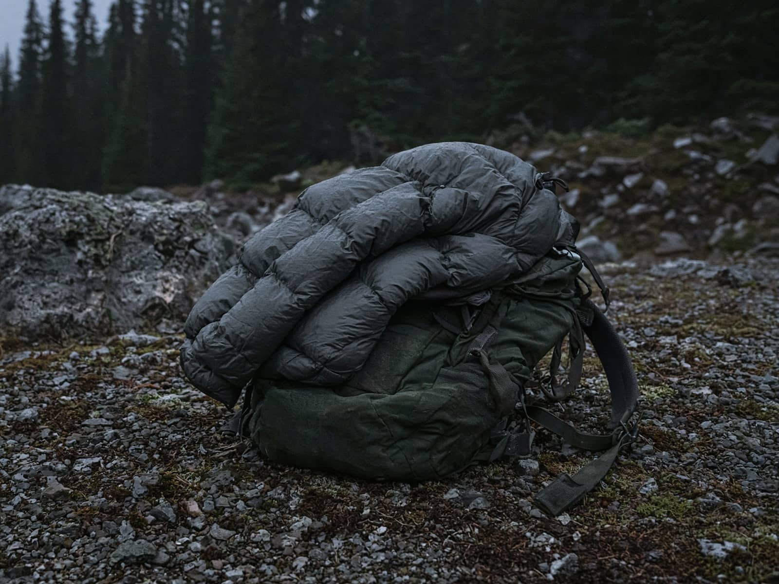 An ultralight down jacket stuffed in its pocket draped over a pack at a cold camp