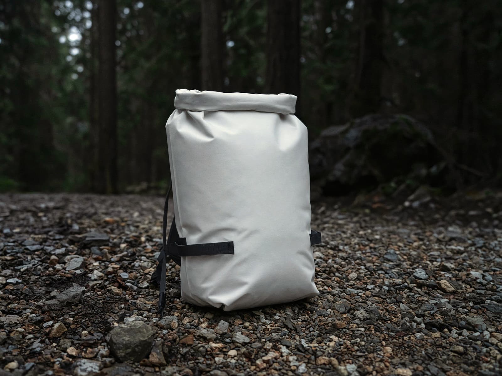 A white waterproof roll-top pack standing on trailhead gravel