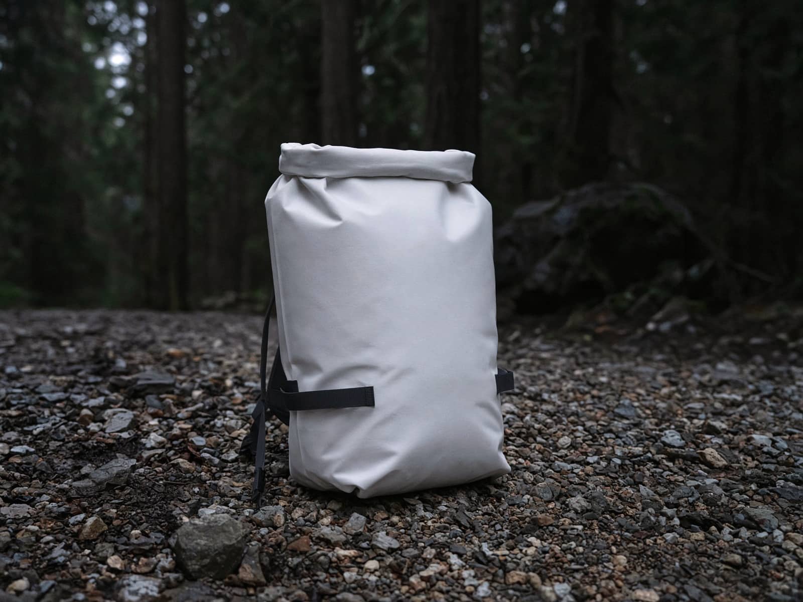 A white waterproof roll-top pack standing on trailhead gravel
